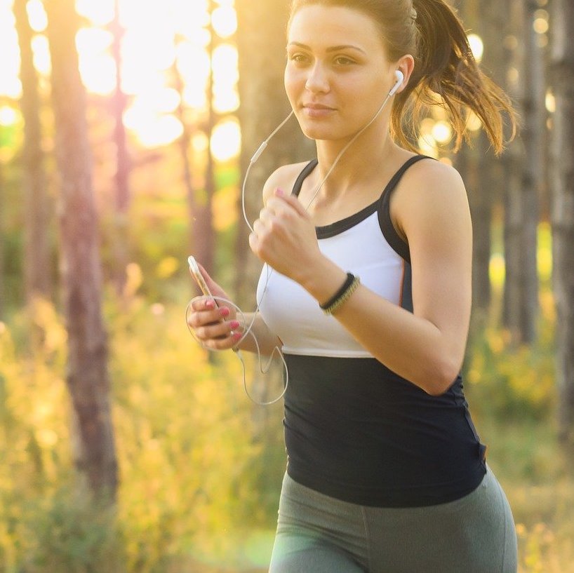 Eine Joggerin läuft am Morgen bei einem Sonnenaufgang durch den Wald.