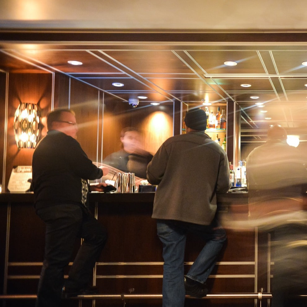 Zwei Männer im Smoking stehen an der Hotelbar zusammen, beide halten ein Glas Champagner in der Hand.
