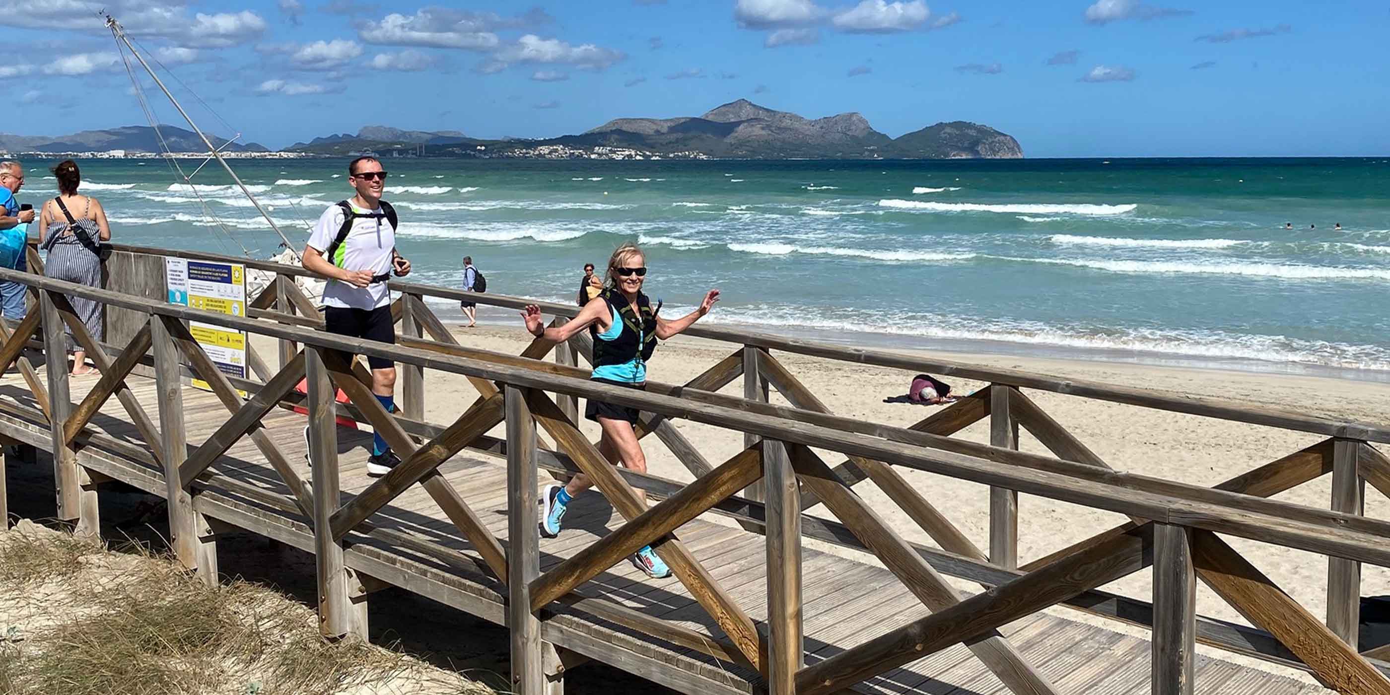 Läuferinnen und Läufer laufen bei einem Mallorca Laufcamp am Strand von Can Picafort über einen Holzsteg