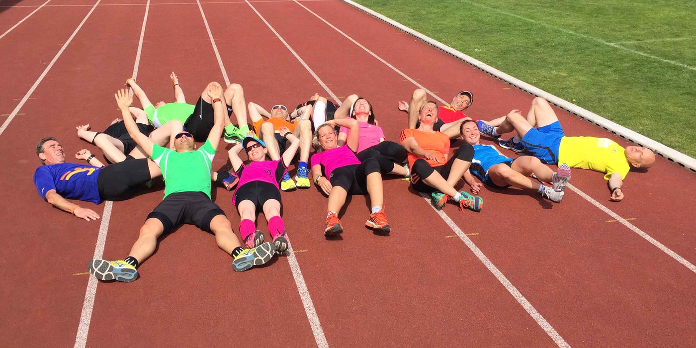 Eine Gruppe liegt müde auf der Tartanbahn. Trainingspläne für die Zwischensaison und Marathon Nachbereitung