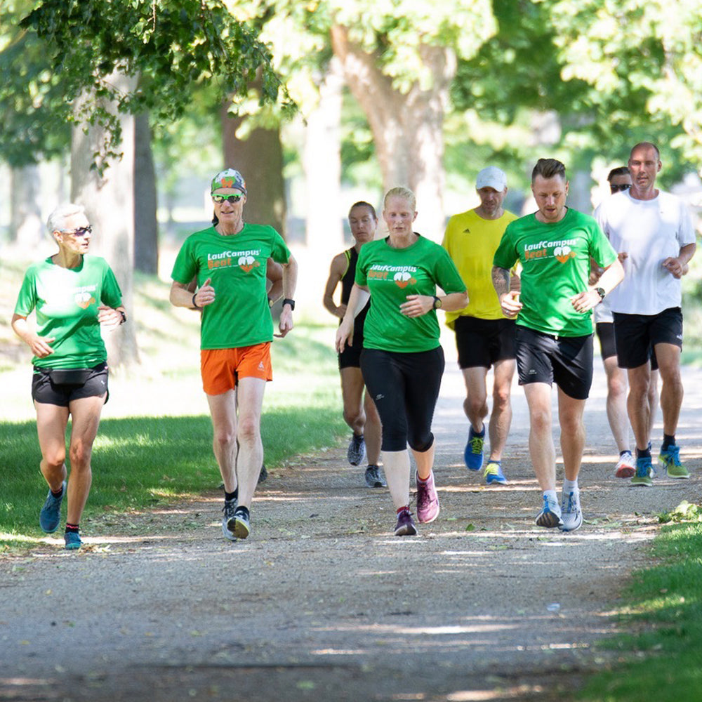 Eine Gruppe Läuferinnen und Läufern läuft beim Laufseminar durch einen Park